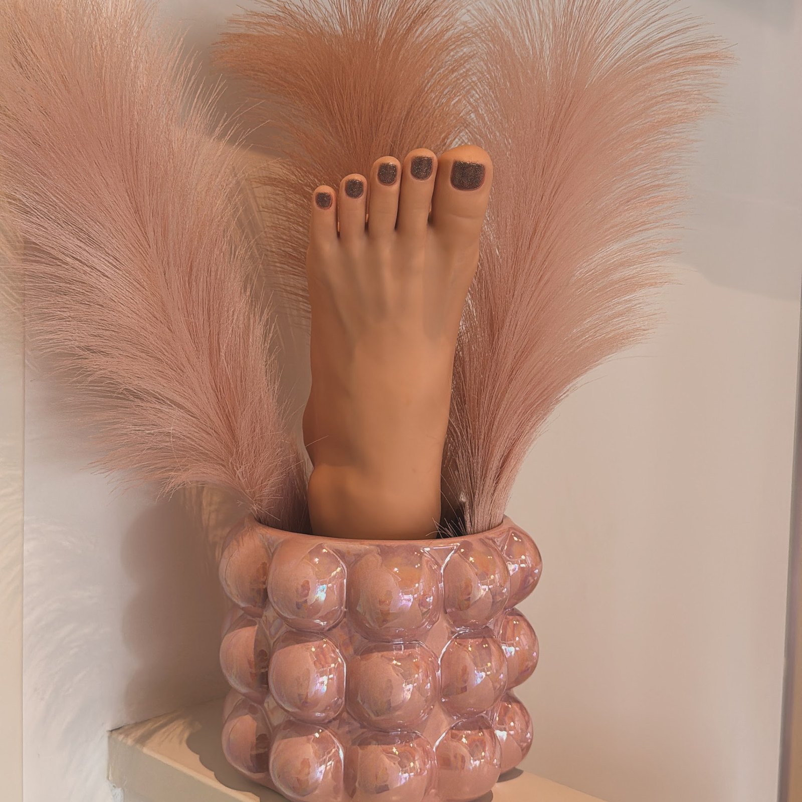 Decoratief voetbeeld met donkere nagellak in een roze vaas met pluimen